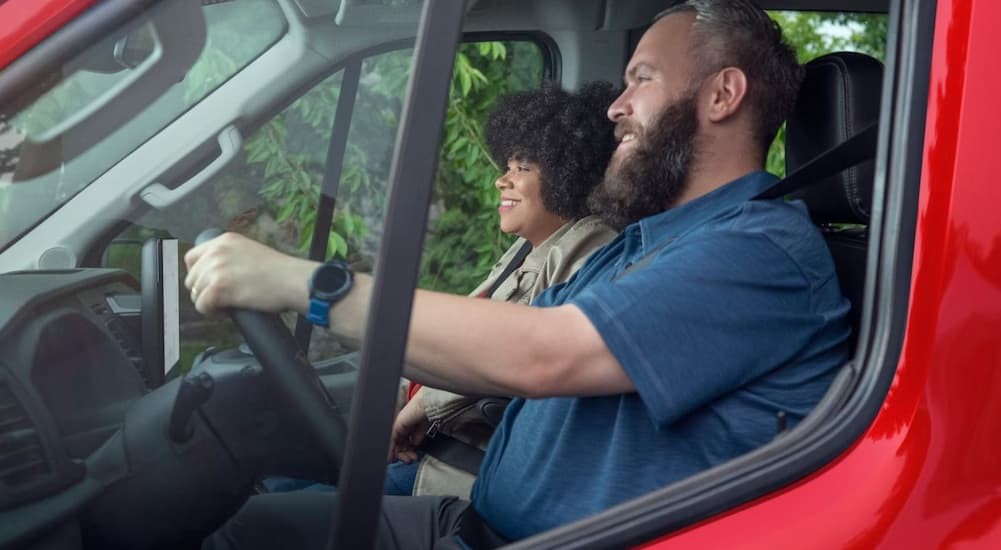 Two people driving in a red 2026 Ford Transit Van.