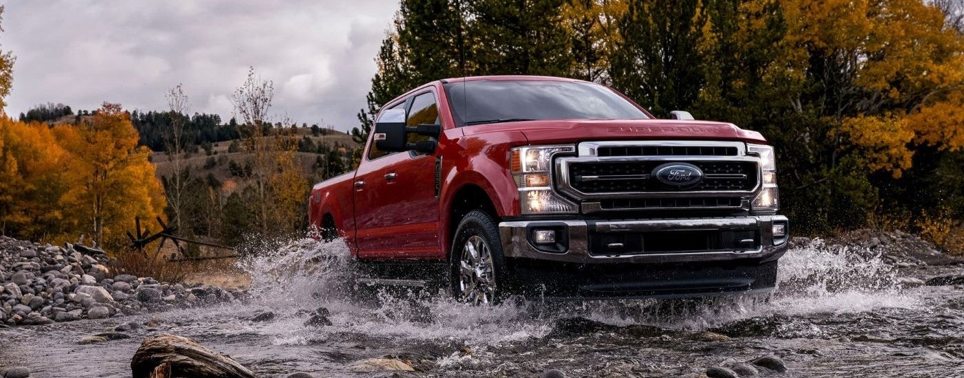 Red 2021 Ford F-250 driving over a shallow river.