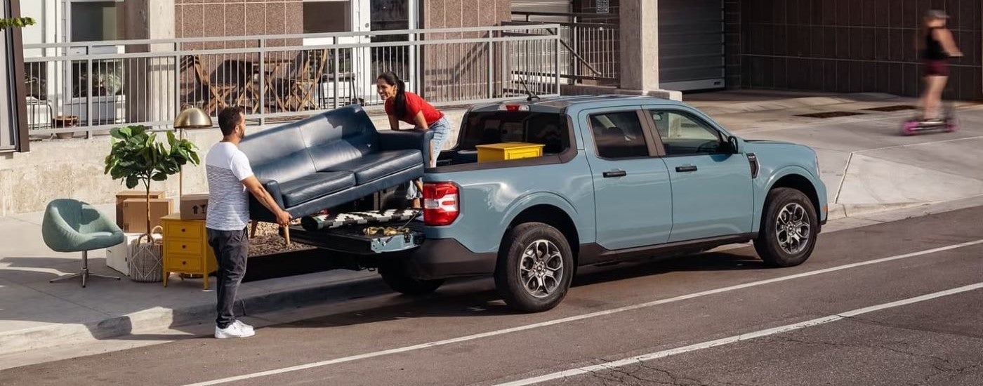 People loading a couch into the bed of a blue 2023 Ford Maverick.