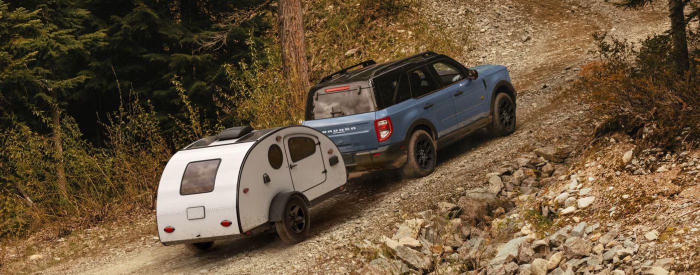 Blue 2026 Ford Bronco Sport towing a camper up a hill off-road.