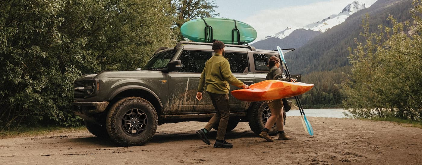 People carrying a kayak from a brown 2026 Ford Bronco parked by a lake.