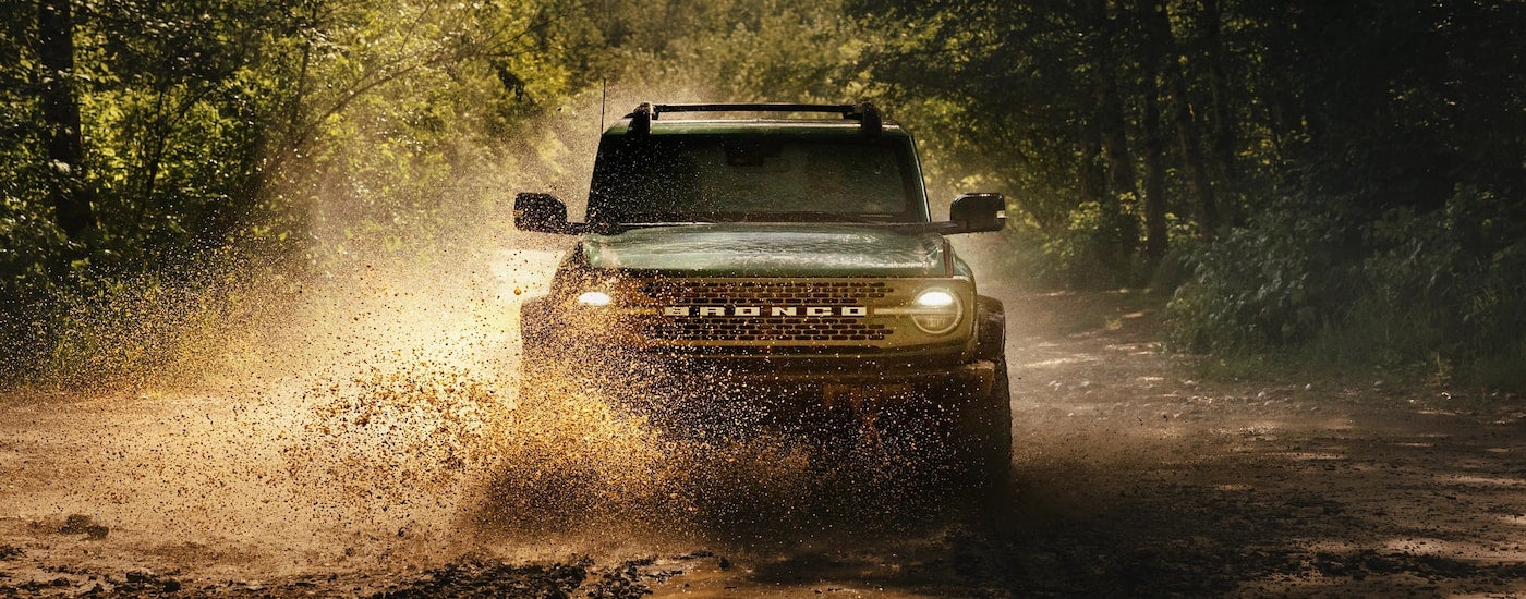 Front of a green 2026 Ford Bronco driving down a trail.