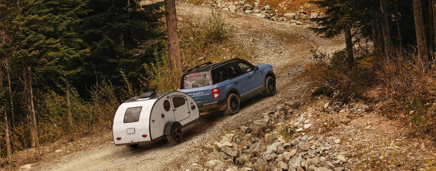 Rear of a blue 2026 Ford Bronco Sport towing a camper up a hill.