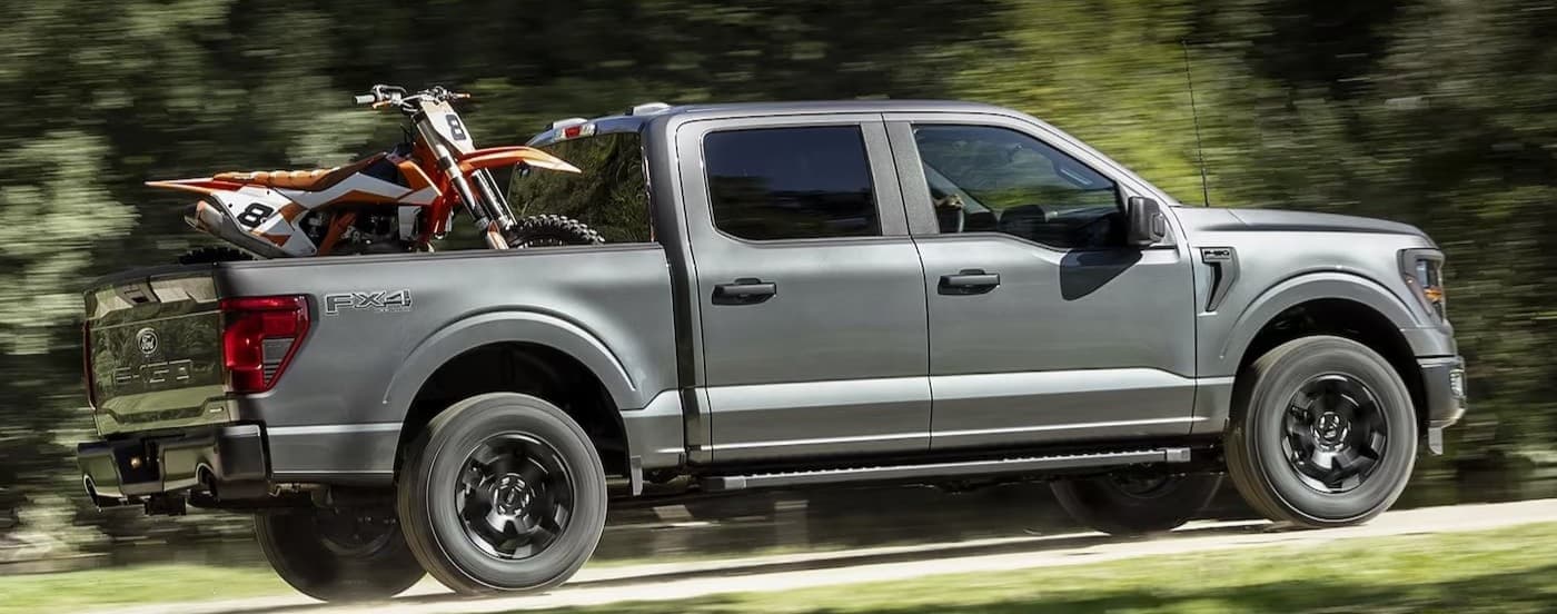 A gray 2024 Ford F-150 driving on a dirt road after visiting a used car dealership.