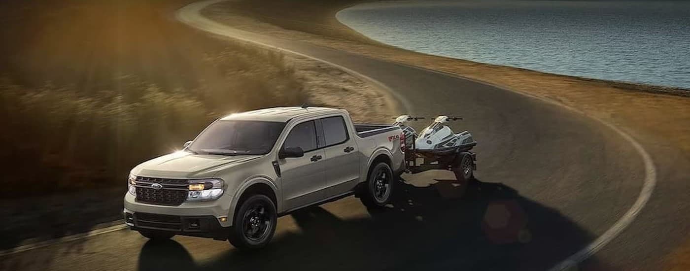 A tan 2024 Ford Maverick towing jetskis on a road.